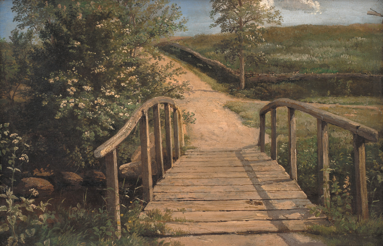 Bild: En enkel smal träbro leder över en liten å. Den fortsatta vägen försvinner i horisonten. Vacker och lugn omgivning med gröna fält och prunkande växter.